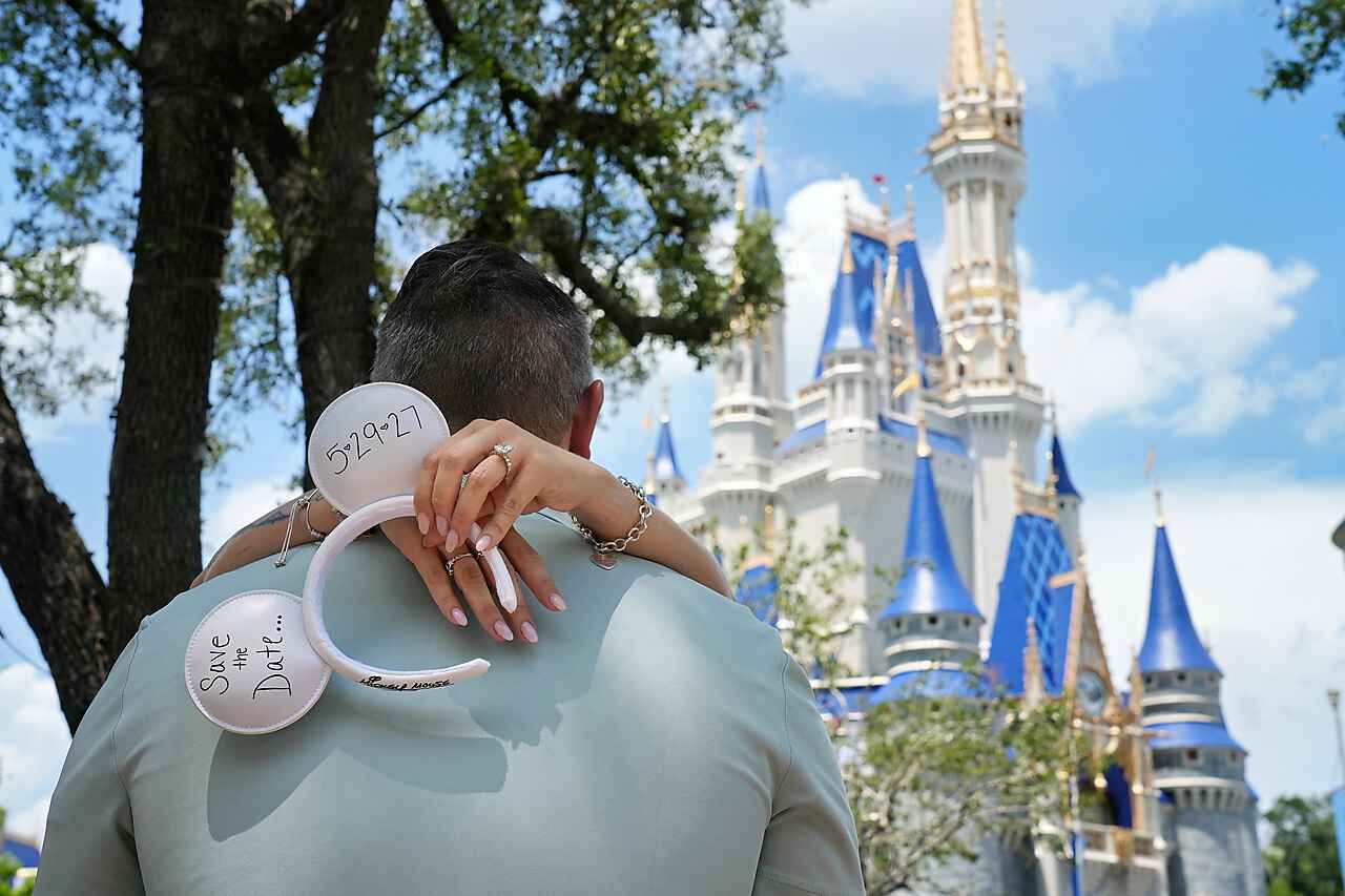 Couple embracing with Save the Date Mickey ears in front of Cinderella Castle