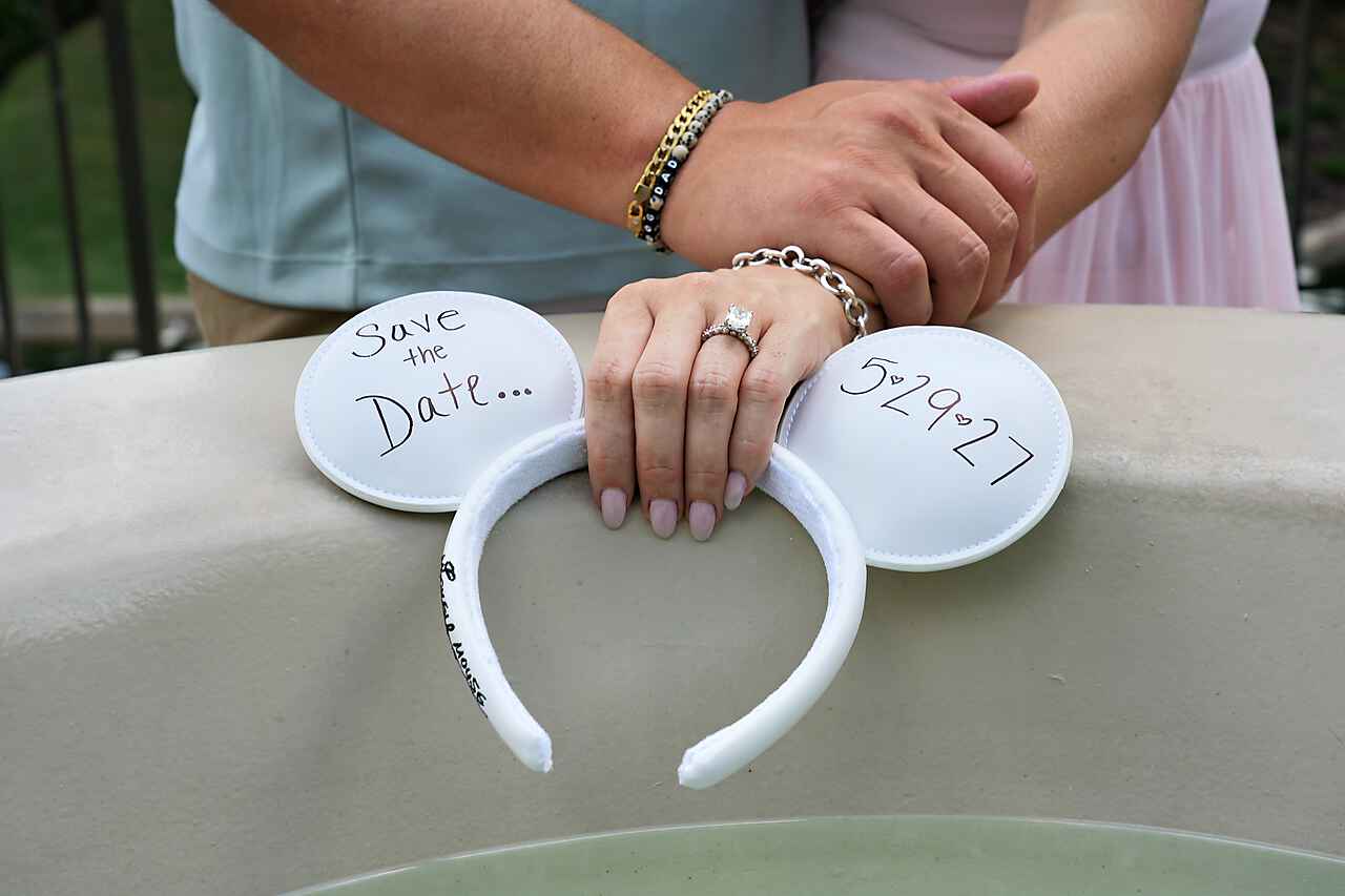Hands resting on Save the Date Mickey ears showing engagement ring